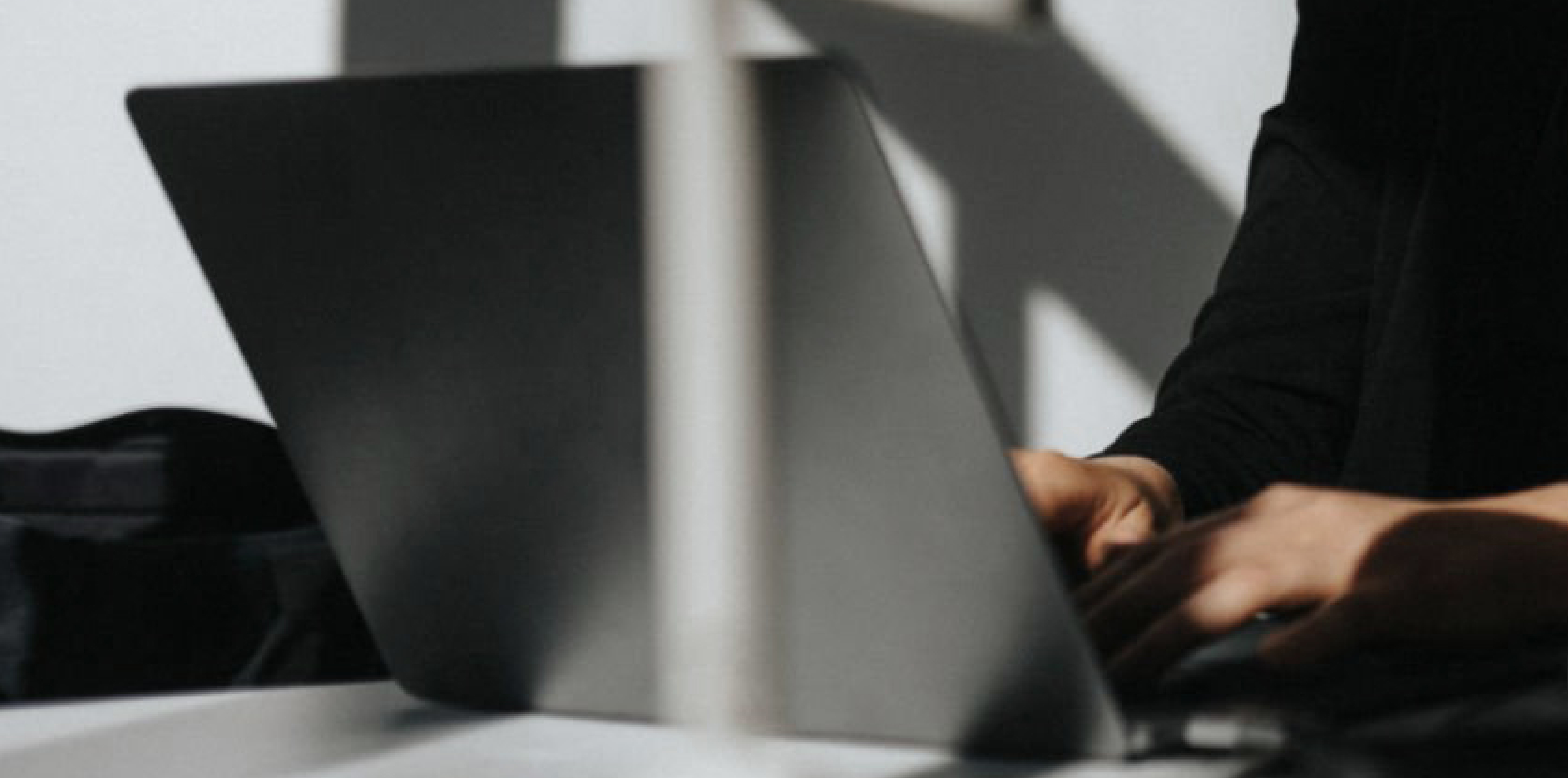 A person working on a sleek laptop in a modern, minimalistic setting with dramatic light and shadow effects, representing focus and digital productivity.