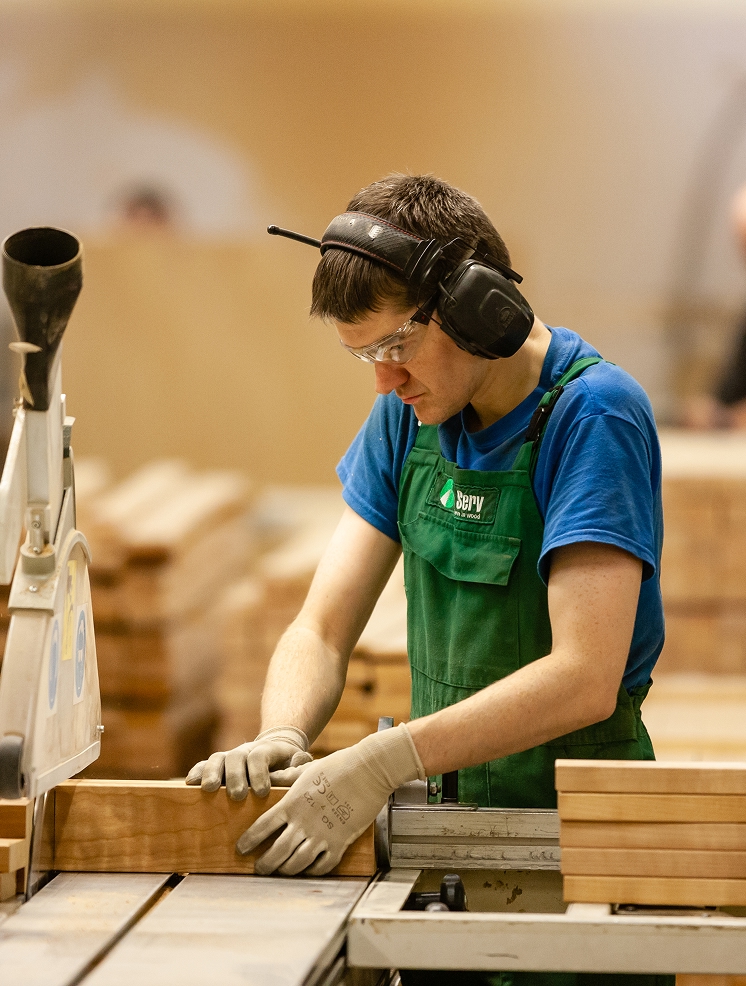 Factory worker in protective gear operating woodworking machinery, representing precision manufacturing and industrial craftsmanship.